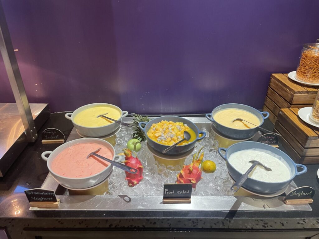 Five bowls of flavored yogurts plus a mixed fruit salad on crushed ice.