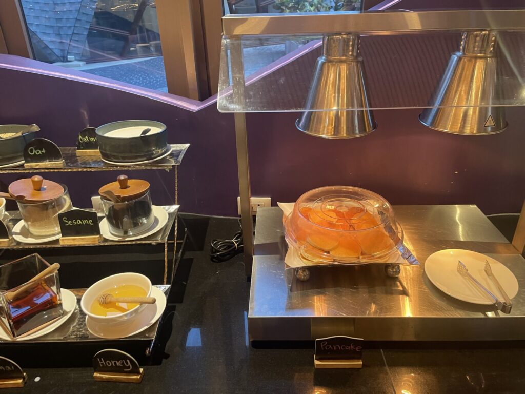 Heat-lamp pancake tray beside honey, oats, and seeds