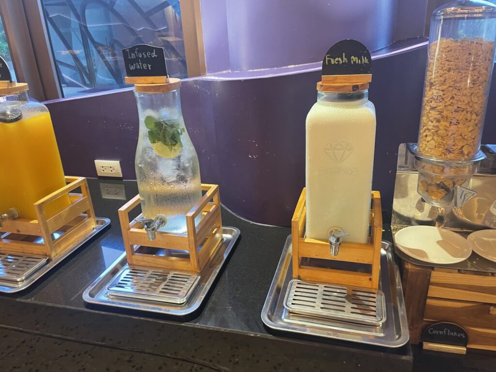 Dispensers of lemon-mint water and chilled fresh milk near cereal.