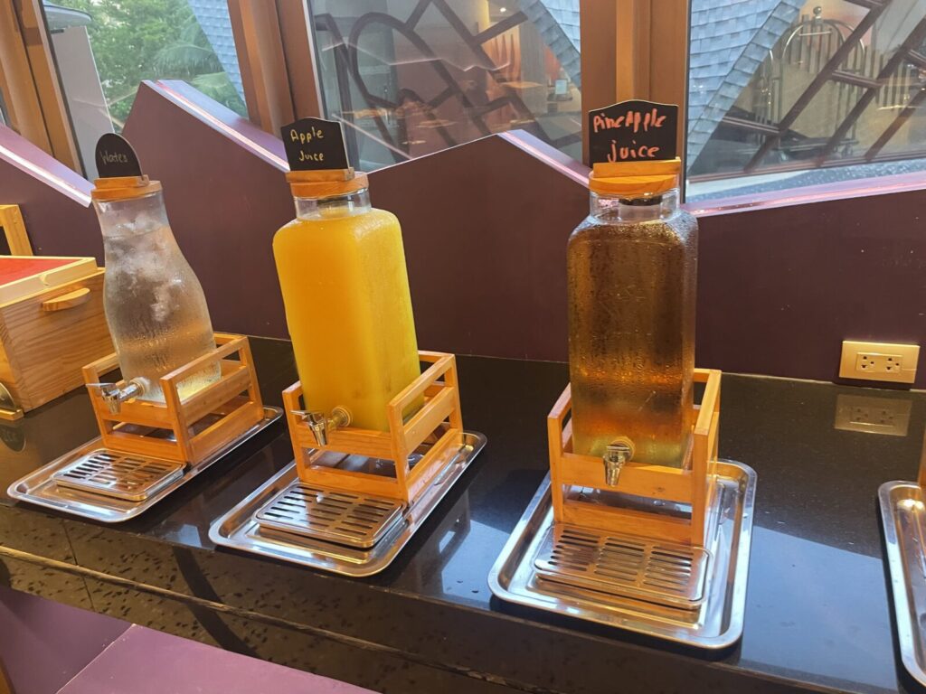 Row of glass drink dispensers labeled water, apple juice, pineapple juice.