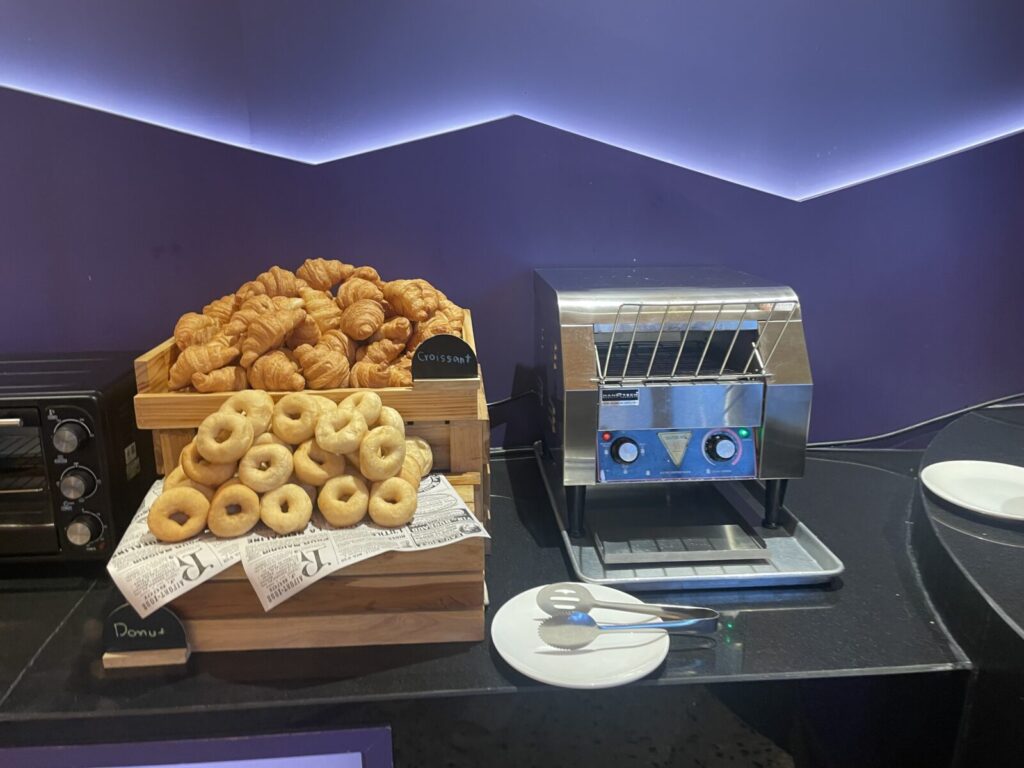 Pile of croissants and plain donuts beside a conveyor toaster