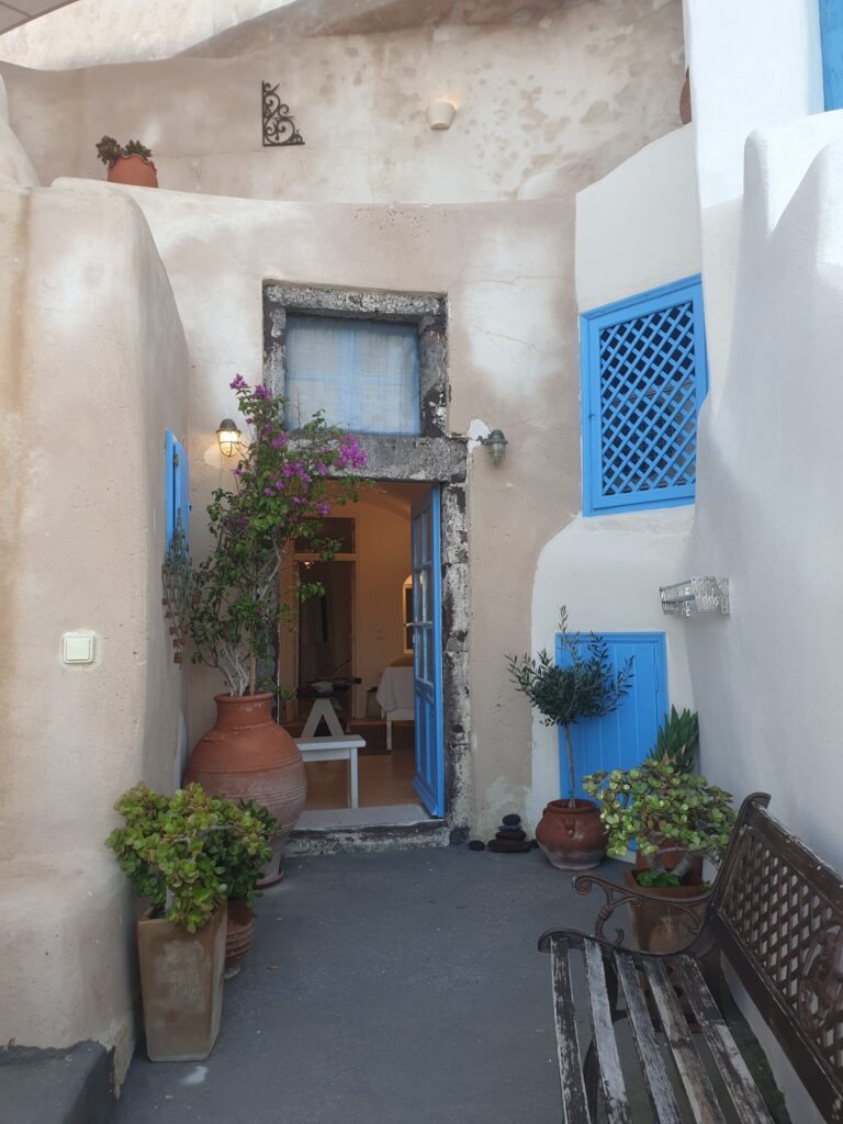 Entrance of Anemi House in Oia, Santorini with blue door, pottery and bougainvillea